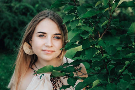 Portrait of a beautiful blonde girl with natural beauty in a green leaves trees. Copy, empty space for text.の写真素材
