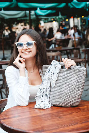 Beautiful young brunette woman wearing in white clothes, holding knitted bag on the background of old wooden doors. Copy, empty space for text.の写真素材