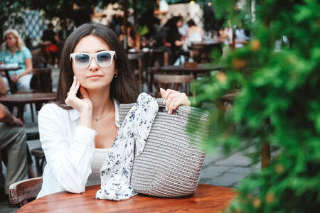 Beautiful young brunette woman wearing in white clothes, holding knitted bag on the background of old wooden doors. Copy, empty space for text.の写真素材