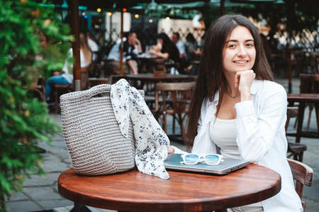 Beautiful young brunette woman wearing in white clothes, holding knitted bag on the background of old wooden doors. Copy, empty space for text.の写真素材