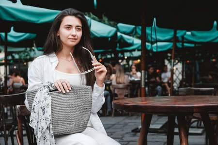Beautiful young brunette woman wearing in white clothes, holding knitted bag on the background of old wooden doors. Copy, empty space for text.の写真素材