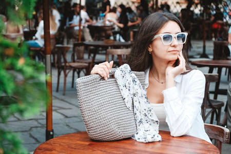 Beautiful young brunette woman wearing in white clothes, holding knitted bag on the background of old wooden doors. Copy, empty space for text.の写真素材