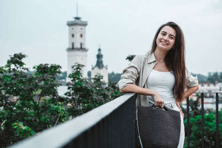 Beautiful young brunette woman wearing in white clothes, holding knitted bag on the background of old wooden doors. Copy, empty space for text.の写真素材