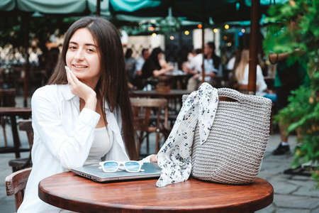 Beautiful young brunette woman wearing in white clothes, holding knitted bag on the background of old wooden doors. Copy, empty space for text.の写真素材