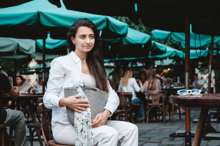 Beautiful young brunette woman wearing in white clothes, holding knitted bag on the background of old wooden doors. Copy, empty space for text.の写真素材