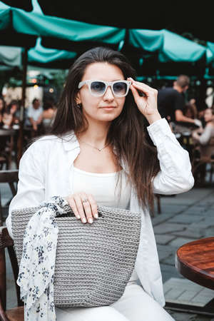 Beautiful young brunette woman wearing in white clothes, holding knitted bag on the background of old wooden doors. Copy, empty space for text.の写真素材