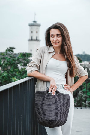 Beautiful young brunette woman wearing in white clothes, holding knitted bag on the background of...