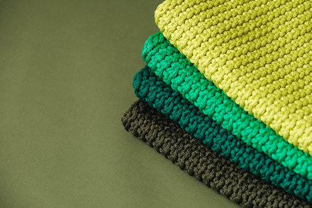 Stack of knitted material from threads of yellow, green, brown colors on a green background. Copy,...