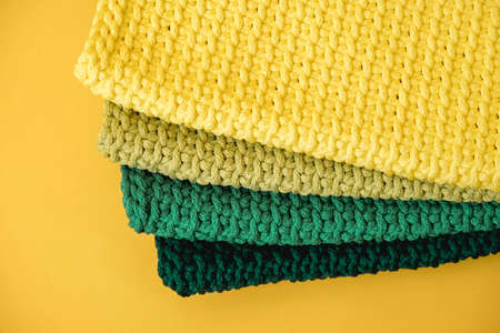 Stack of knitted material from threads of yellow, green, brown colors on a green background. Copy, empty space for text.の写真素材