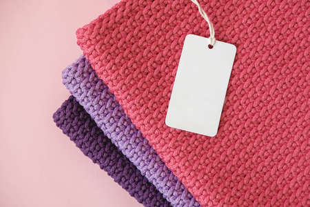 Stack of knitted material from threads of pink, red, purple colors with blank Price Tag on a pink background. Top view. Copy, empty space for text.の写真素材