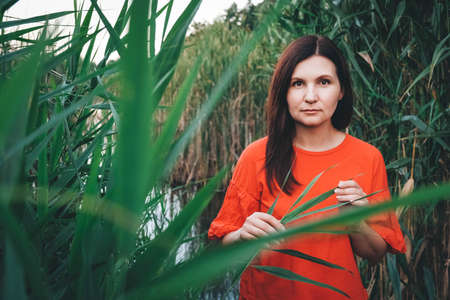 Portrait of a beautiful woman dressed in red clothes standing against the backdrop of reeds and lake. Copy, empty space for text.の写真素材