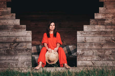Portrait of a beautiful woman in a straw hat dressed in red clothes on a background of reeds and lake. Copy, empty space for text.の写真素材