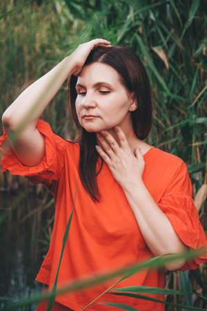 Portrait of a beautiful woman in a straw hat dressed in red clothes on a background of reeds and lake. Copy, empty space for text.の写真素材