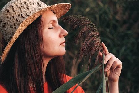 Portrait of a beautiful woman in a straw hat dressed in red clothes on a background of reeds and lake. Copy, empty space for text.の写真素材