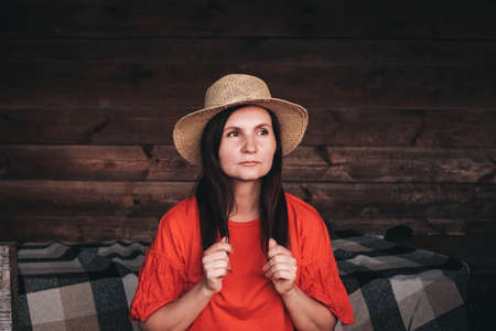 Portrait of a beautiful woman in a straw hat dressed in red clothes on a background of reeds and lake. Copy, empty space for text.の写真素材
