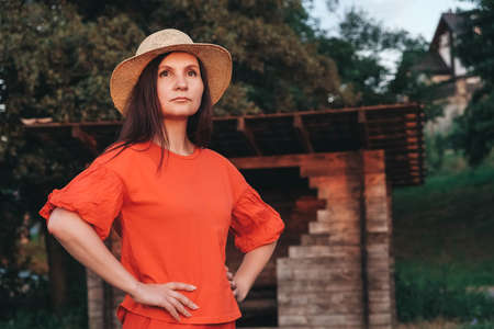 Beautiful woman in a straw hat dressed in red clothes on a background of reeds and lake. Copy, empty space for text.の写真素材