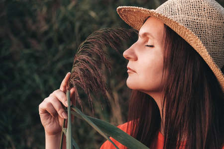 Beautiful woman in a straw hat dressed in red clothes on a background of reeds and lake. Copy, empty space for text.の写真素材