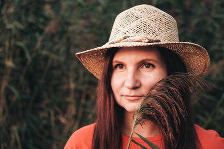 Beautiful woman in a straw hat dressed in red clothes on a background of reeds and lake. Copy, empty space for text.の写真素材