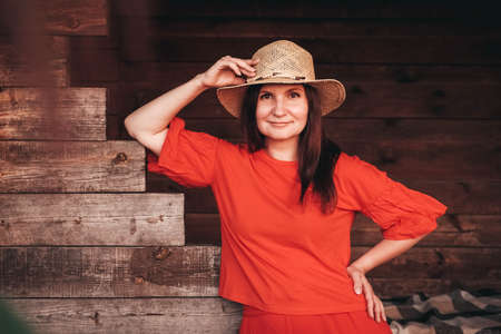 Beautiful woman in a straw hat dressed in red clothes on a background of reeds and lake. Copy, empty space for text.の写真素材