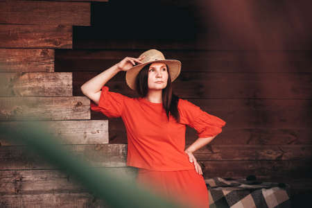 Beautiful woman in a straw hat dressed in red clothes on a background of reeds and lake. Copy, empty space for text.の写真素材