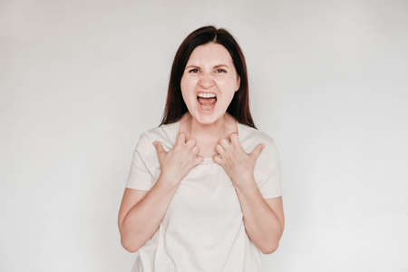 Shocked panic brunette woman dressed in casual white t shirt pulls her hands by her hair and screaming in despair and frustration, her eyes full of terror, mouth open. Copy, empty space for text.の写真素材