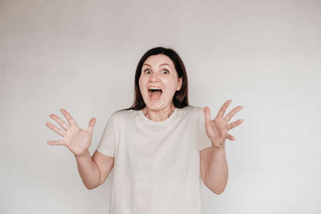 Shocked panic brunette woman dressed in casual white t shirt pulls her hands by her hair and screaming in despair and frustration, her eyes full of terror, mouth open. Copy, empty space for text.の写真素材