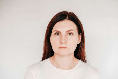 Shocked panic brunette woman dressed in casual white t shirt pulls her hands by her hair and screaming in despair and frustration, her eyes full of terror, mouth open. Copy, empty space for text.の写真素材