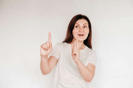 Shocked panic brunette woman dressed in casual white t shirt pulls her hands by her hair and screaming in despair and frustration, her eyes full of terror, mouth open. Copy, empty space for text.の写真素材
