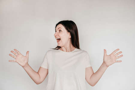 Shocked panic brunette woman dressed in casual white t shirt pulls her hands by her hair and screaming in despair and frustration, her eyes full of terror, mouth open. Copy, empty space for text.の写真素材