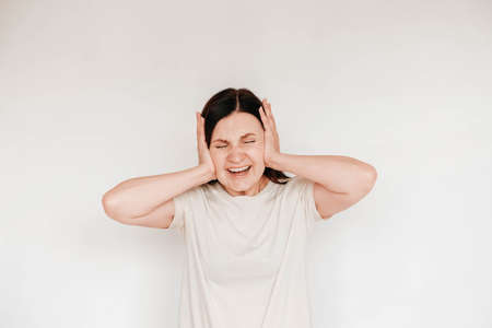 Shocked panic brunette woman dressed in casual white t shirt pulls her hands by her hair and screaming in despair and frustration, her eyes full of terror, mouth open. Copy, empty space for text.の写真素材