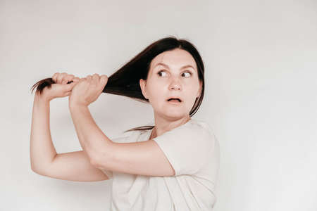 Shocked panic brunette woman dressed in casual white t shirt pulls her hands by her hair and screaming in despair and frustration, her eyes full of terror, mouth open. Copy, empty space for text.の写真素材