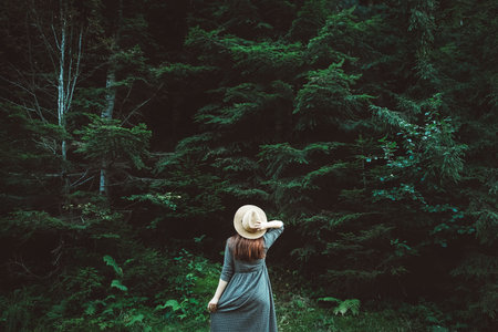 Beautiful red-haired young woman in a straw hat and dress on a background of green forest and trees. Place for text or advertising.の写真素材