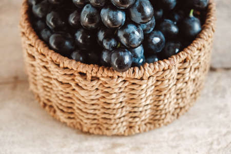 Bunch of black grapes in a round wicker basket on a old wooden table. Top view. Copy, empty space for text.の写真素材