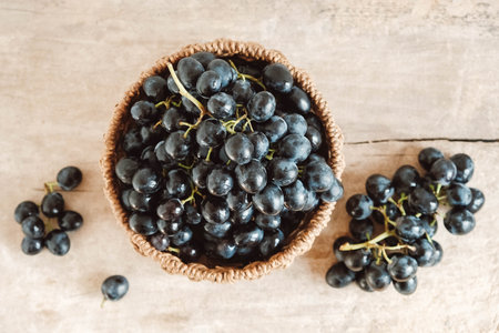 Bunch of black grapes in a round wicker basket on a old wooden table. Top view. Copy, empty space for text.の写真素材