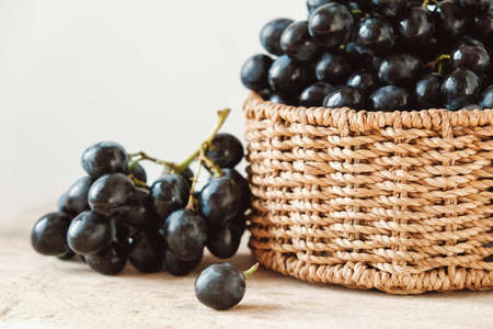 Bunch of black grapes in a round wicker basket on a old wooden table. Copy, empty space for text.の写真素材