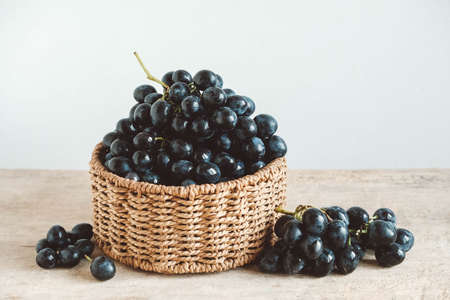 Bunch of black grapes in a round wicker basket on a old wooden table. Copy, empty space for text.の写真素材