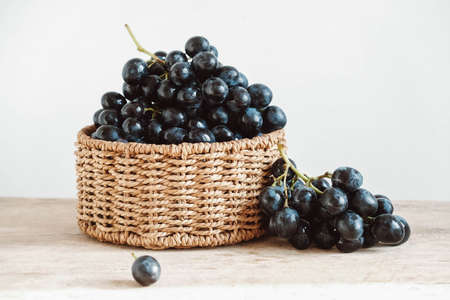 Bunch of black grapes in a round wicker basket on a old wooden table. Copy, empty space for text.の写真素材