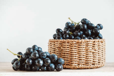 Bunch of black grapes in a round wicker basket on a old wooden table. Copy, empty space for text.の写真素材