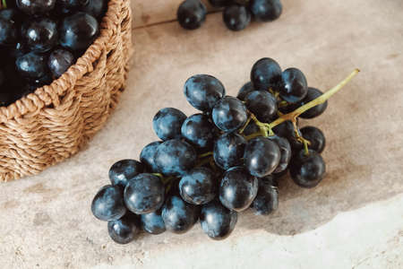 Bunch of black grapes in a round wicker basket on a old wooden table. Copy, empty space for text.の写真素材