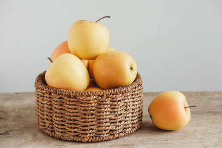 Yellow apples in a round wicker basket on a wooden table. Copy, empty space for text.の写真素材