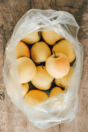 Yellow apples in a plastic bag on a wooden table. Top view. Copy, empty space for text.の写真素材