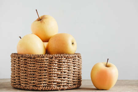 Yellow apples in a round wicker basket on a wooden table. Copy, empty space for text.の写真素材