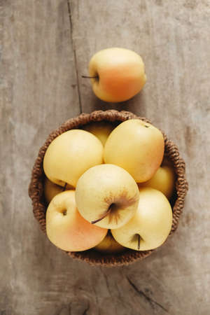 Yellow apples in a round wicker basket on a wooden table. Top view. Copy, empty space for text.の写真素材