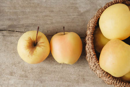 Yellow apples in a round wicker basket on a wooden table. Top view. Copy, empty space for text.の写真素材