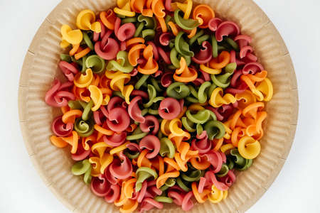 Multicolored pasta in a disposable paper plate on a white background. Top view. Copy, empty space for text.の写真素材