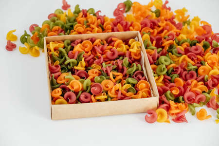 Multicolored pasta in a cardboard box scattered on a white background. Top view. Copy, empty space for text.の写真素材