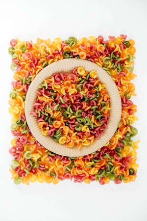 Multicolored pasta in a disposable paper plate on a white background. Top view. Copy, empty space for text.の写真素材