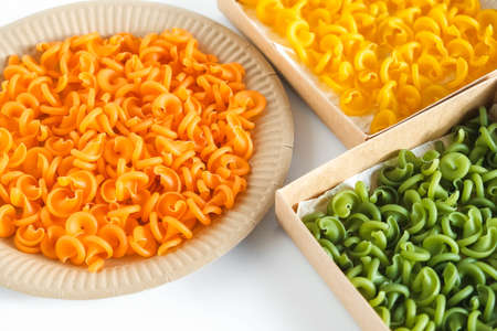 Multicolored pasta in a disposable kraft paper plates and boxes on a white background. Top view. Copy, empty space for text.の写真素材