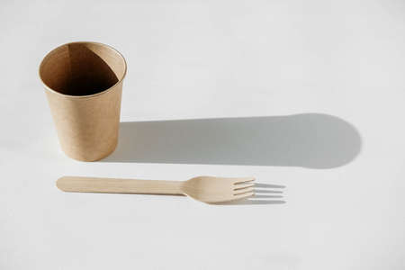 Disposable paper cup and wooden fork with shadow from light on a white background. Copy, empty space for text.の写真素材