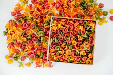 Multicolored pasta in a cardboard box scattered on a white background. Top view. Copy, empty space for text.の写真素材